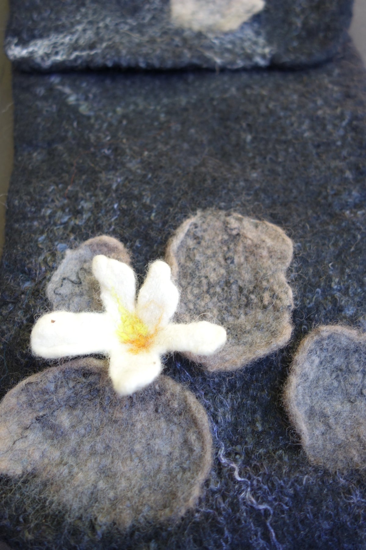 Close-up of white flower and felted stone details on hand-felted crossbody bag